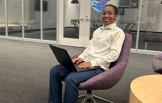 Mya Zylberberg, UAlbany MS in Digital Forensics and Cybersecurity Student, smiles and poses for a photo while seated in a chair holding an open laptop.
